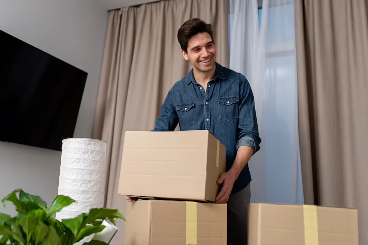 Smiling man lifting cardboard boxes in a bright living room, representing stress-free moving services by