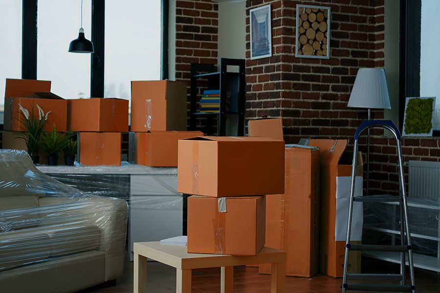 Office space filled with packed cardboard boxes, furniture wrapped in plastic, and a stepladder, illustrating