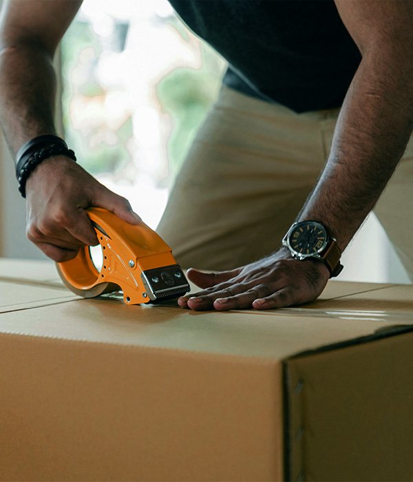 Person using packing tape dispenser to seal a cardboard box, emphasizing careful packing for a