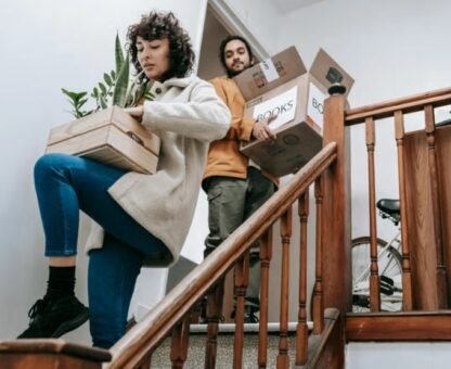 People carefully moving plants and boxes up stairs during a house removal.